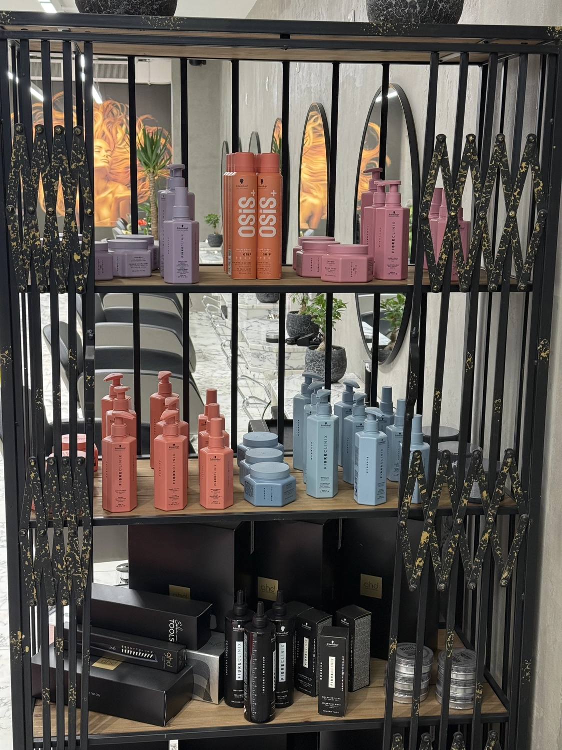 Ein schwarzes Metallregal, in dem verschiedene Haarpflegeprodukte in rosa, blauen, orangen und schwarzen Flaschen und Behältern ausgestellt sind, darunter Marken wie Siso und Fibre Clinix.