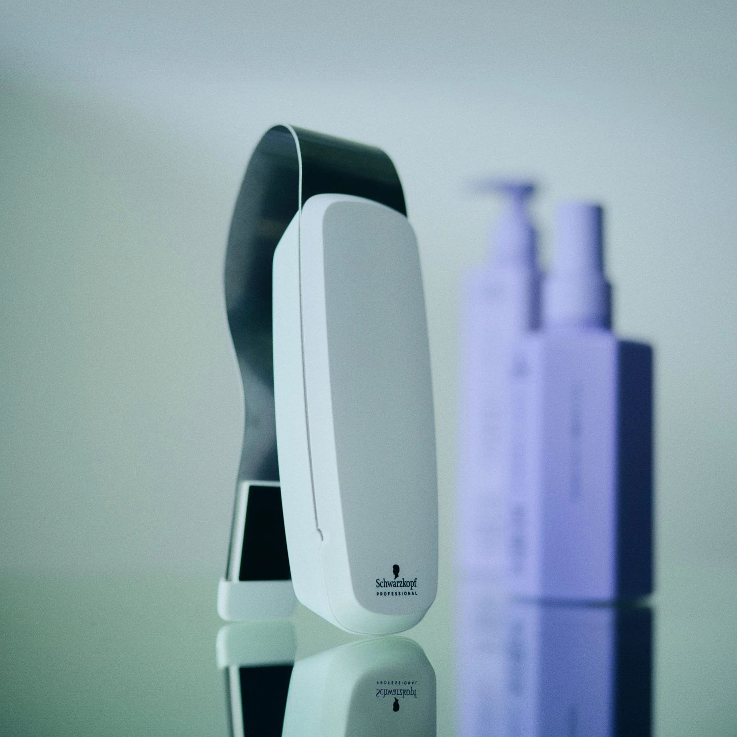 Hairfashion by Edmond - Haarschnitt und Styling - Ein weißes, handliches Haaranalysegerät steht aufrecht neben mehreren Flaschen mit lila und schwarzen Haarpflegeprodukten auf einer Ablagefläche.